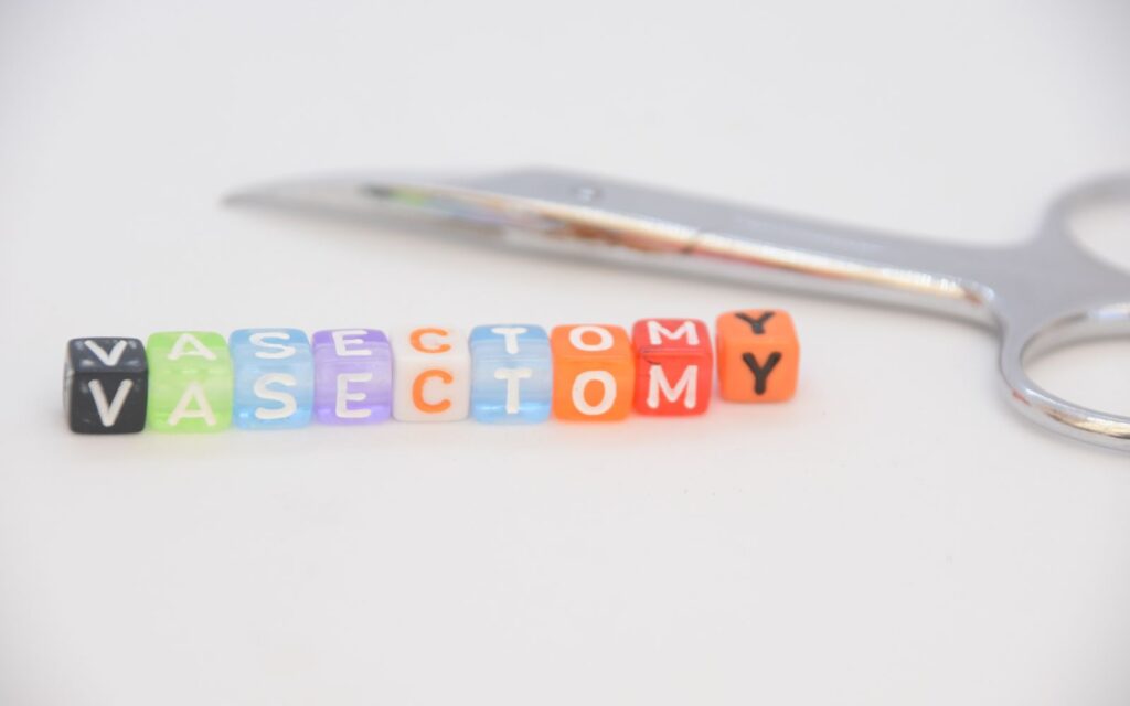 Dice spelling "VASECTOMY INSURANCE" with surgical scissors in background.