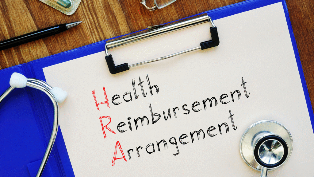 Clipboard on a wooden desk with "Health Reimbursement Arrangement" written in red and black ink, accompanied by a stethoscope, pen, glasses, and medicine, symbolizing healthcare funding.