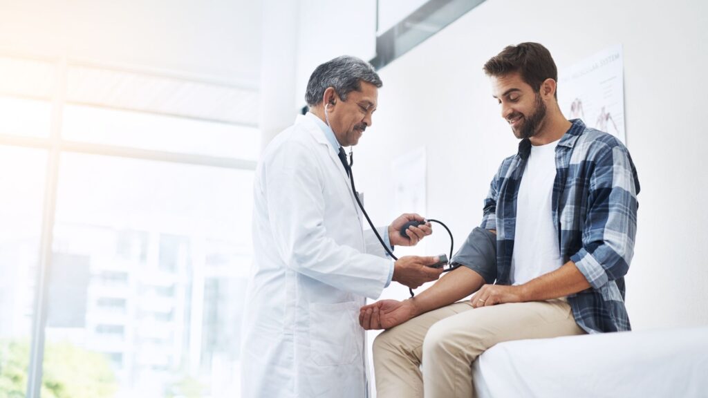 A doctor measures a young man's blood pressure in a bright medical office, showcasing a routine health check-up.